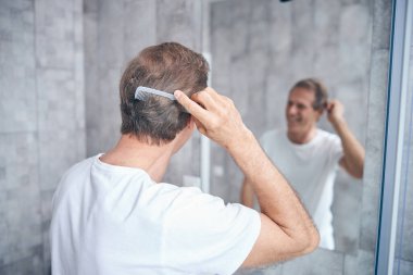 Taraklı bir adam aynaya bakıyor.