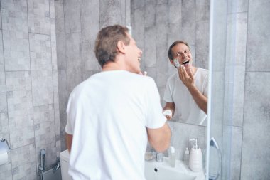 Traş köpüğü kullanan neşeli yetişkin bir erkek.