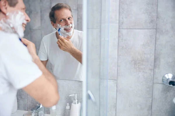 Pleased male shaving himself in the bathroom