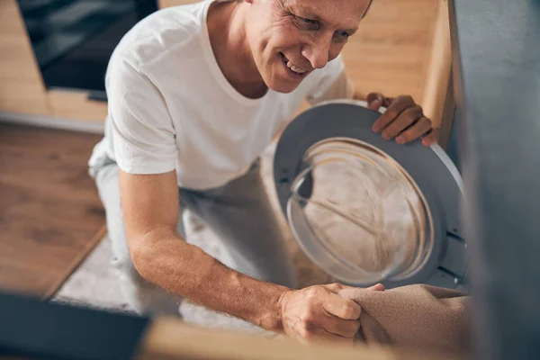 Εστιασμένη φωτογραφία στον χαρούμενο άντρα που κοιτάζει το πλυντήριο. — Φωτογραφία Αρχείου