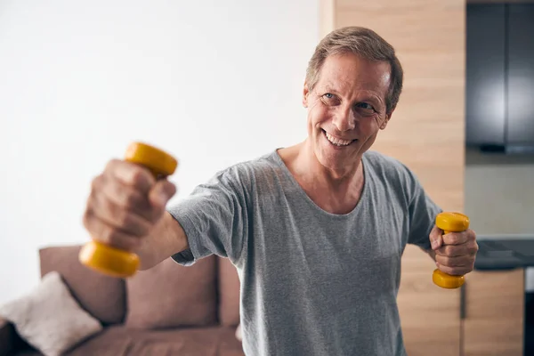 Kind mature man lifting dumbbells with pleasure — Stock Photo, Image