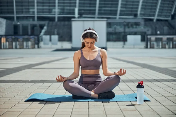 Mulher relaxada em fones de ouvido fazendo ioga fora — Fotografia de Stock