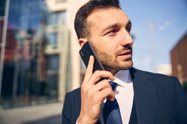 Genç beyaz adam dışarıda cep telefonuyla konuşuyor.