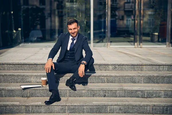Ευτυχισμένος μελαχρινός επιχειρηματίας κάθεται έξω κοντά στο γραφείο — Φωτογραφία Αρχείου