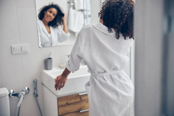 Potěšená dáma dotýká své vlasy před zrcadlem — Stock fotografie