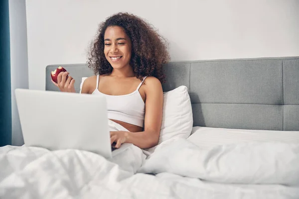 Sorridente donna utilizzando il suo computer a letto — Foto Stock