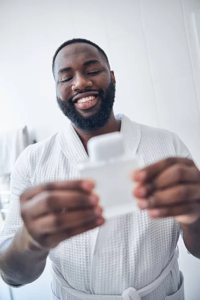 Hombre alegre de piel oscura mirando su frasco de perfume — Foto de Stock