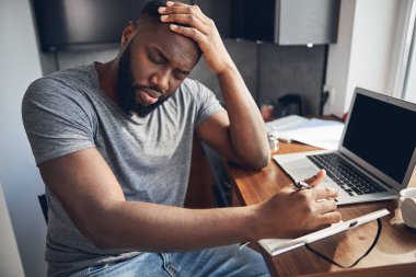 Genç esmer adam kafasına dokunuyor.