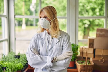 Koruyucu maskeli bir biyolog başka tarafa bakıyor.