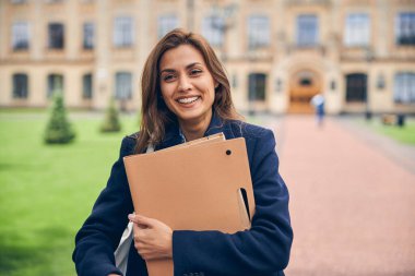 Üniversitenin yanında klasörler tutan mutlu güzel kız.