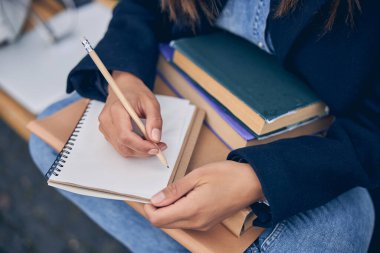 Bahar kıyafetleri içindeki kadın dizlerinde kitap tutuyor.