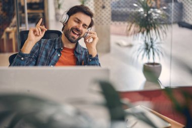 Neşeli genç adam iş yerinde müzik dinliyor.