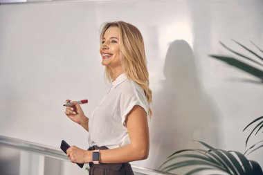 Ofiste beyaz tahtanın yanında duran neşeli genç bayan.