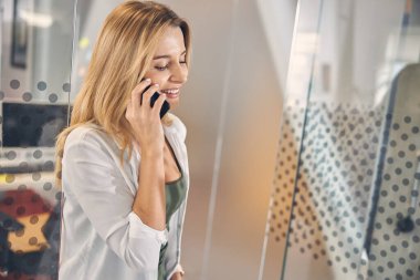 Ofiste cep telefonuyla konuşan neşeli bayan işçi.