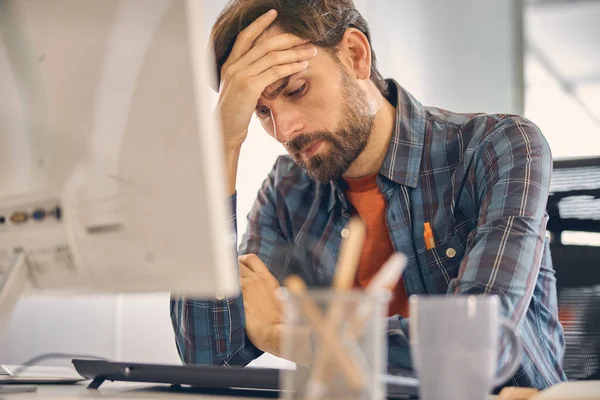 En utmattad ung man som använder dator på jobbet — Stockfoto