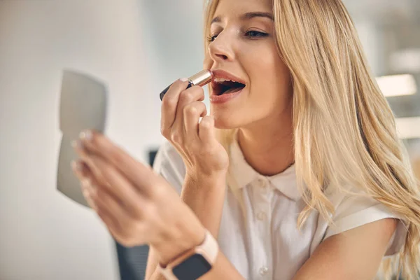 Attractive young woman putting on lipstick at work — Stock Photo, Image