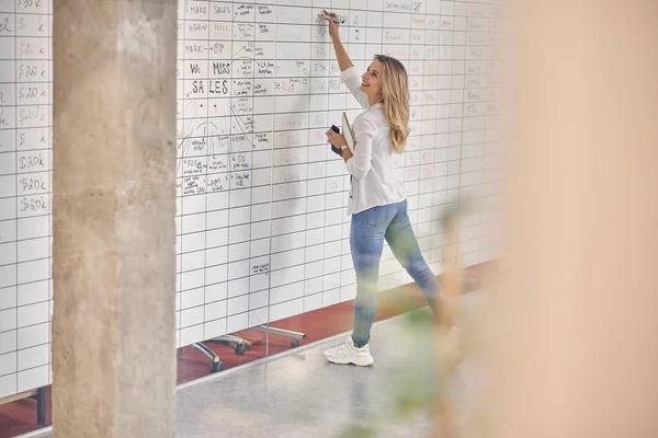 Wesoła młoda kobieta pisząca na tablicy w biurze — Zdjęcie stockowe