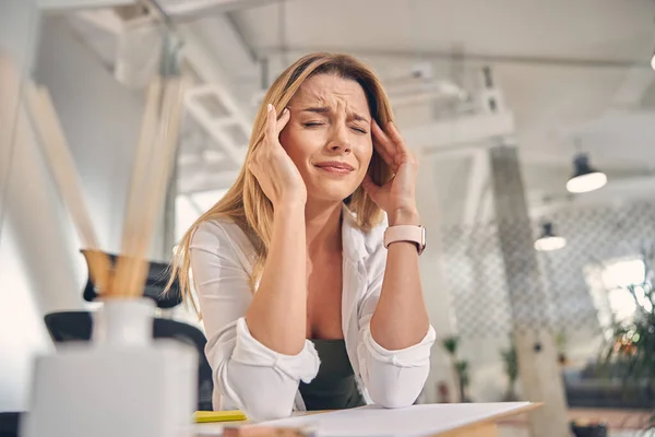 Overwerkte jonge vrouw met hoofdpijn op het werk — Stockfoto