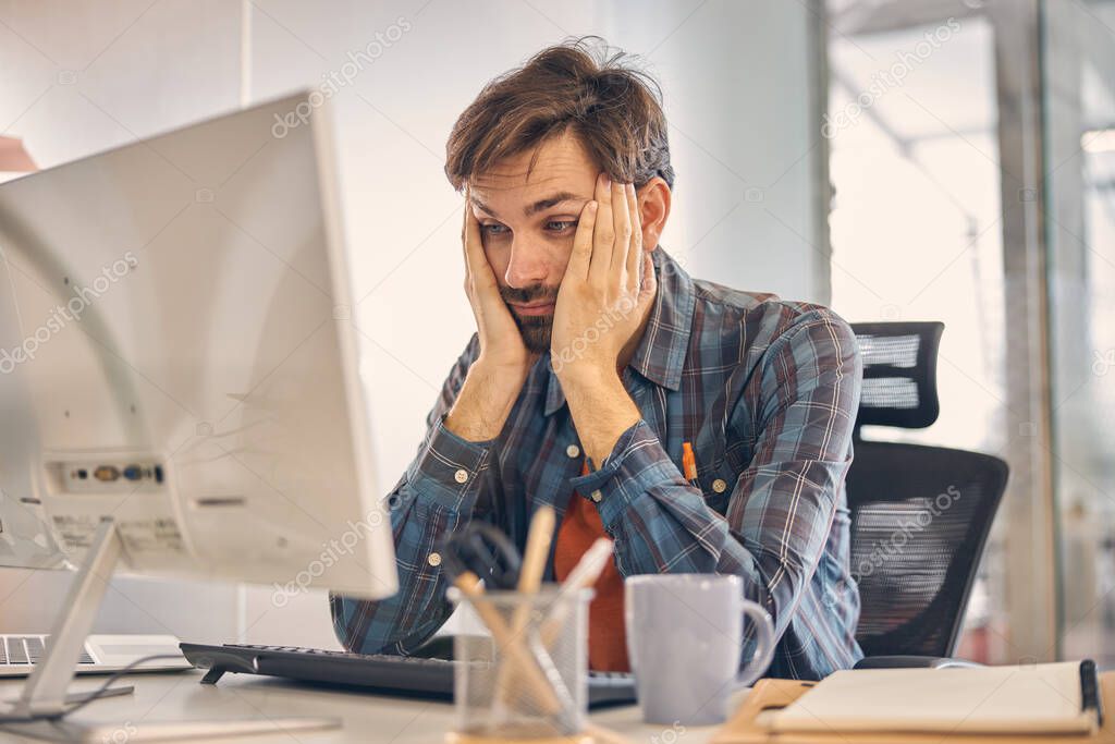 Exhausted male worker using computer in office