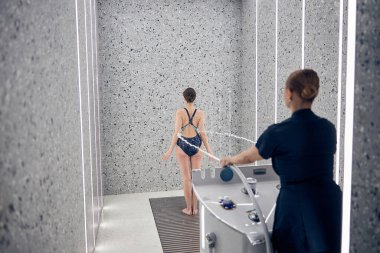 Kadın hasta çıplak ayakla paspasın üzerinde duruyor.