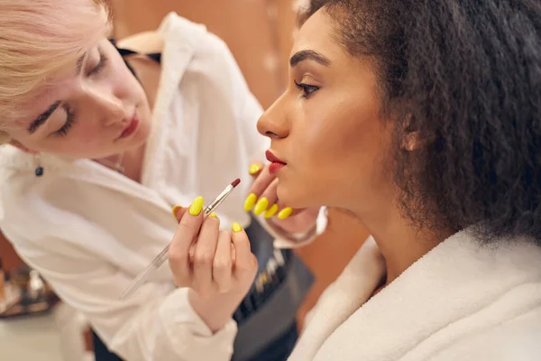 Dygtige skønhedskunstner gør makeup til charmerende kvinde - Stock-foto