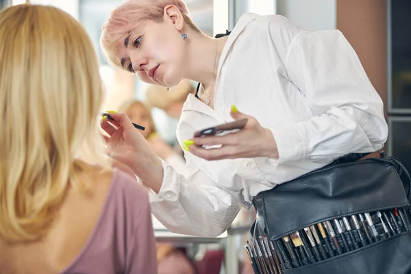 Estilista concentrada haciendo maquillaje para su cliente — Foto de Stock