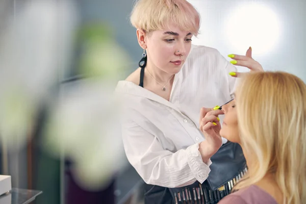 Jovem pessoa feminina atenciosa fazendo maquiagem no salão — Fotografia de Stock