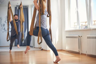 Koyu renk saçlı yoga öğretmeni ve öğrencisi birlikte egzersiz yapıyor.