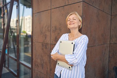 Dizüstü bilgisayarını iki eliyle sıkı tutan memnun bayan.
