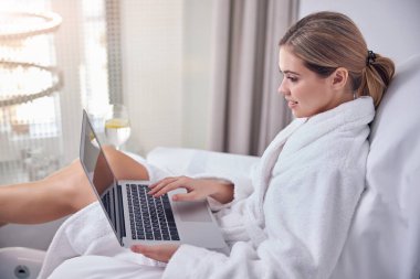 Spa salonunda dizüstü bilgisayar kullanan mutlu genç bir kadın.