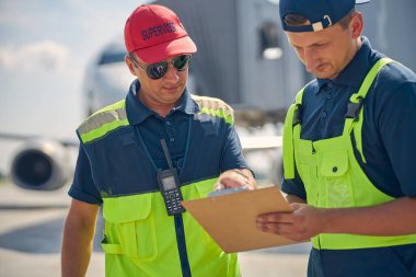 Bir belgeyi inceleyen iki konsantre havaalanı çalışanı