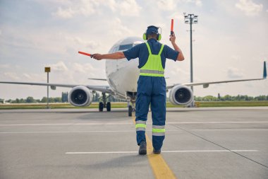Adam pilota marshalling çubuklarıyla işaret veriyor.