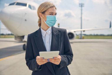 Yüzü maskeli bir havaalanı çalışanı başka tarafa bakıyor.