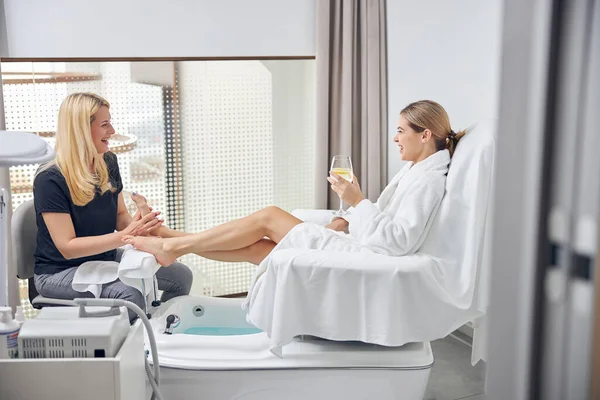 Vrolijke dame communiceren met vrouwelijke schoonheidsspecialiste tijdens voet massage — Stockfoto
