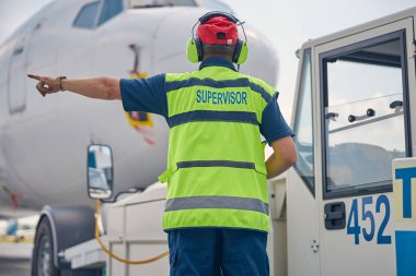 Denetmen bir elini sola doğru gösteriyor.