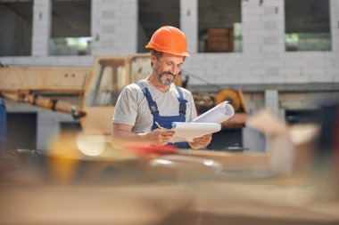 Gülümseyen çekici erkek müteahhit ev planlarını inceliyor.