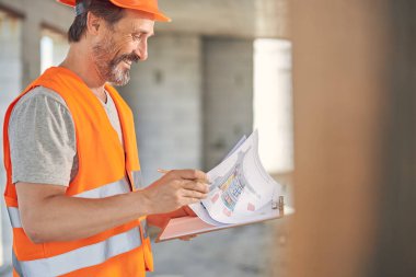 Yansıtıcı yelekli bir adam planlarını inceliyor.