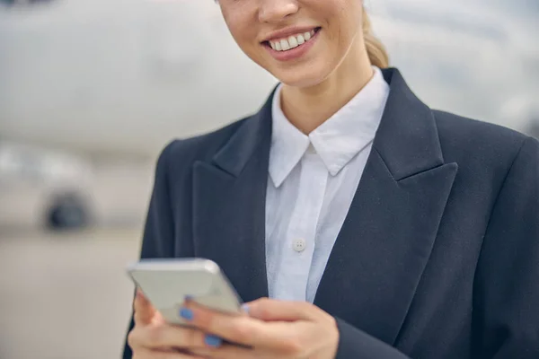 Agradable empleado femenino del aeropuerto sosteniendo un teléfono inteligente — Foto de Stock