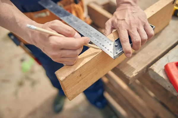 Carpintero midiendo la longitud en un lado de la madera — Foto de Stock