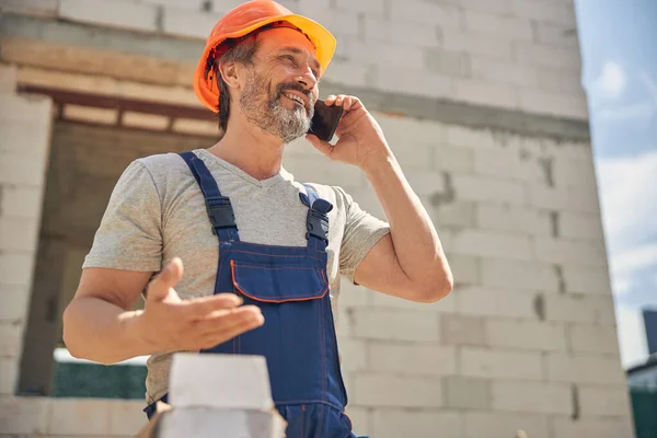 Joyous construtor maduro usando seu smartphone ao ar livre — Fotografia de Stock