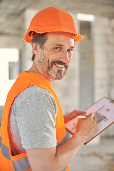 Kasklı sakallı bir adam elinde planlar tutuyor.