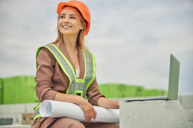 Gülümseyen modern beyaz kadın mühendis dışarıda oturuyor.