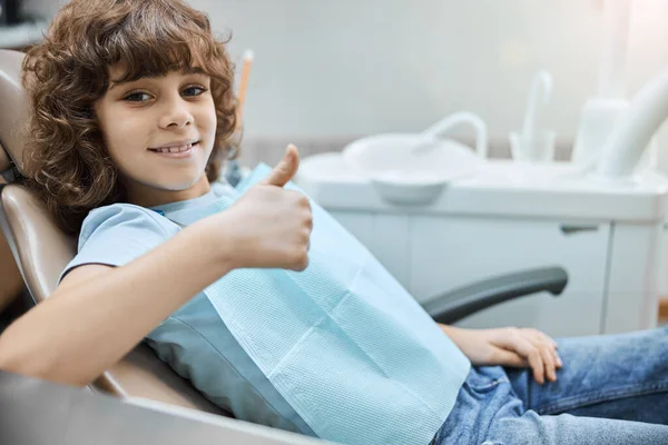 Pozitivně vypadající kluk držící palce nahoru na zubní klinice — Stock fotografie