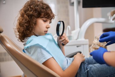 Dişleri öğrenmek için büyüteç kullanan meraklı bir çocuk.