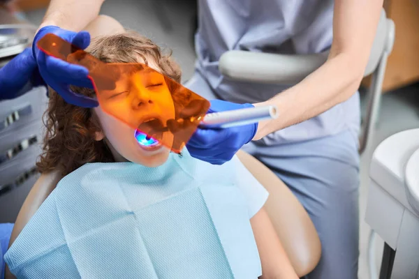 Çocuk dişçi koltuğunda oturuyor ve diş macunu ile tedavi ediliyor. — Stok fotoğraf