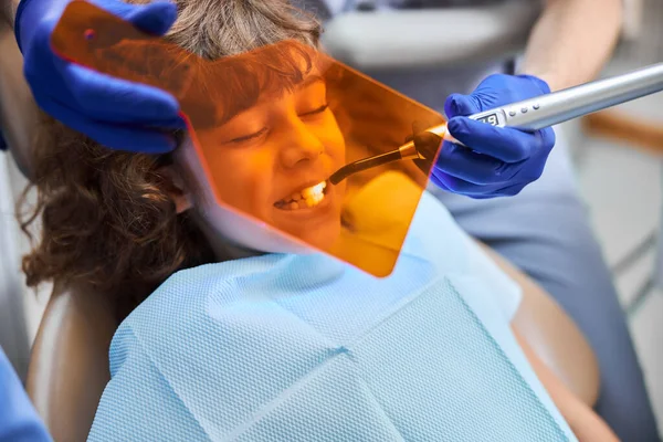 Ребенок сидит в стоматологическом кресле с оранжевым экраном рядом с лицом — стоковое фото