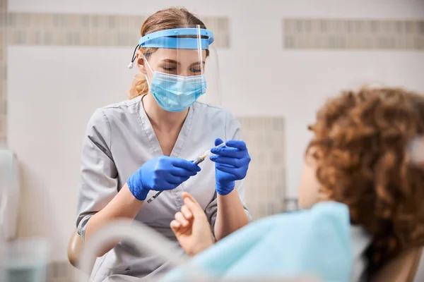 Spécialiste dentaire ouvrant une seringue pendant le traitement d'un enfant — Photo
