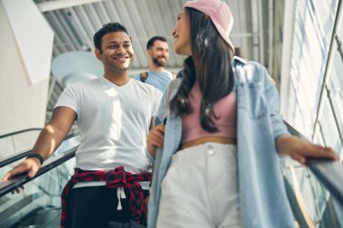 Yakışıklı Hintli erkek, hareketli merdivenlerde dikilirken şık bir kadını dinliyor.