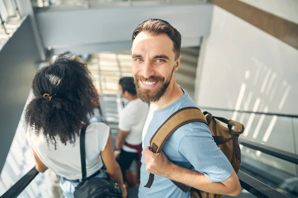 Feliz sorriso barbudo homem em movimento escadaria no aeroporto internacional — Fotografia de Stock