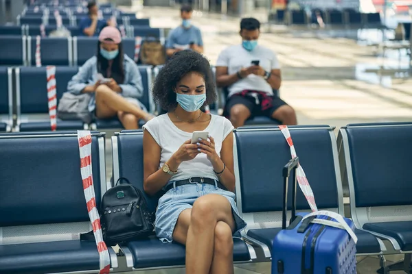 Egy nő mobilt használ a reptéren, a padon ül. — Stock Fotó